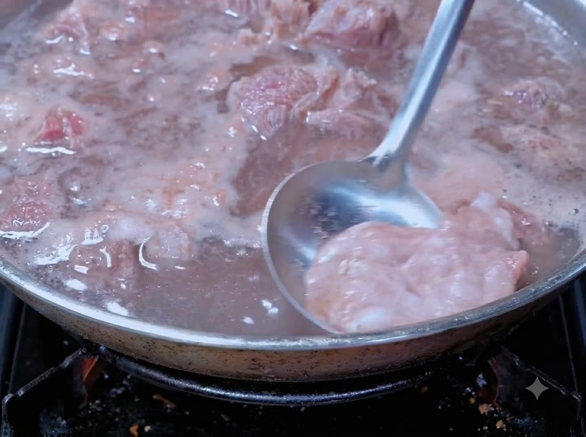 調理中の鍋で、煮立つ牛肉からお玉を使って血のアクをすくい取っている様子。
