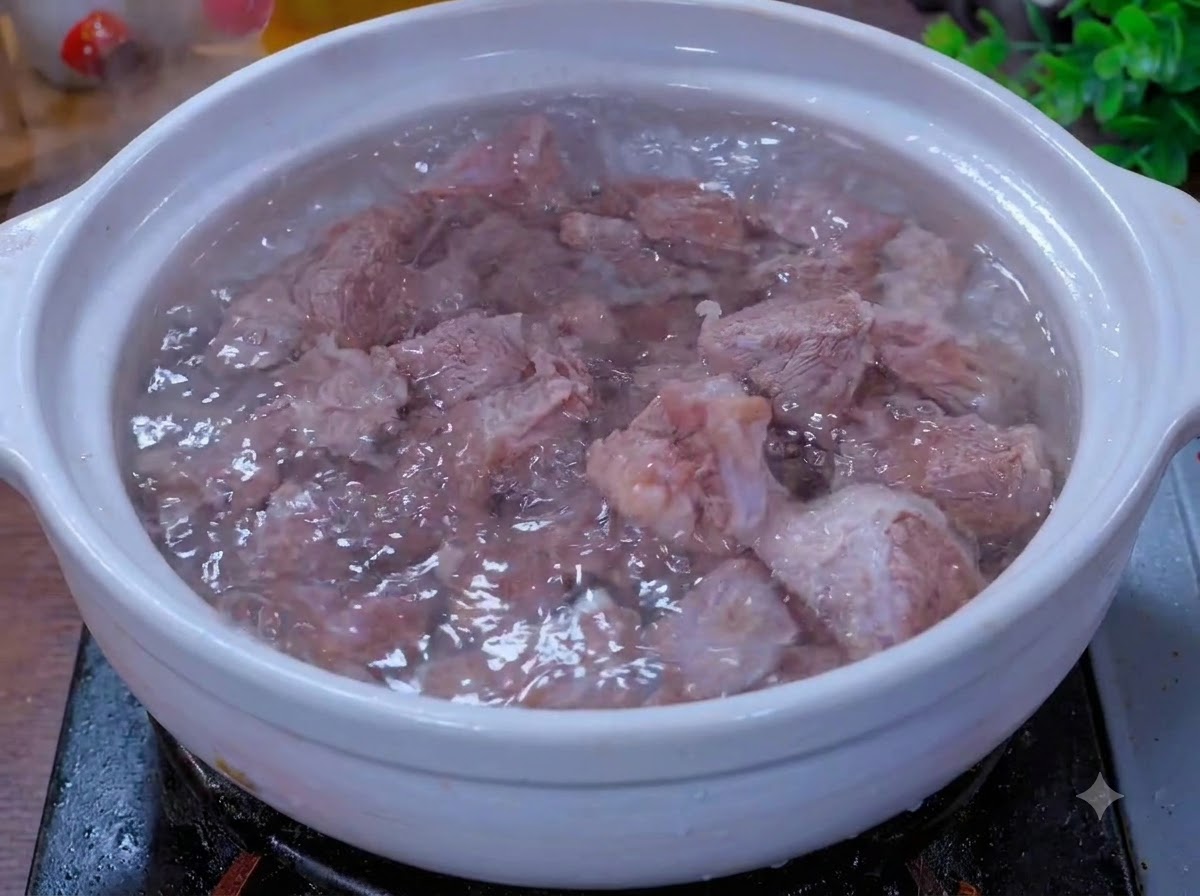 白い土鍋の中で、ネギや生姜などの香味野菜と一緒に牛肉の破片が煮込まれている様子。