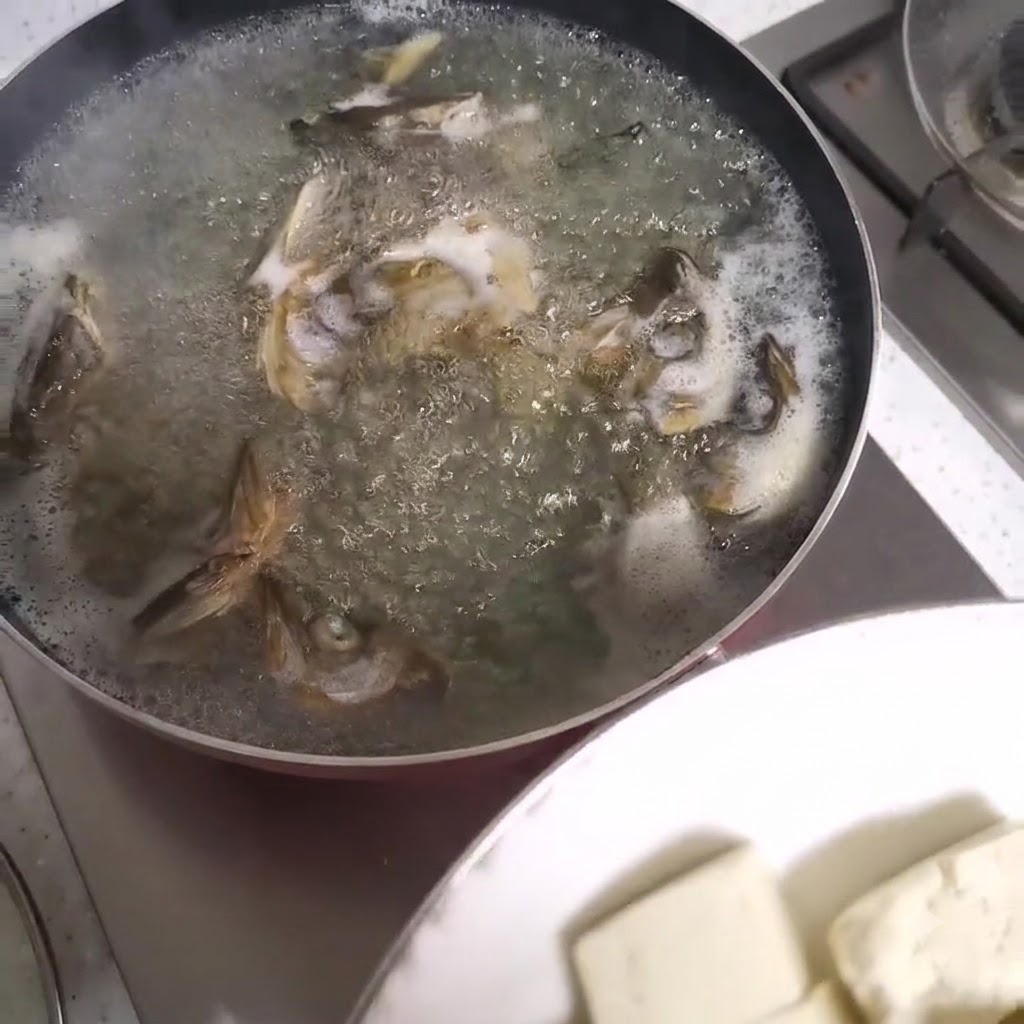 魚のアラースープが沸騰している鍋に、豆腐の角切りが加えられているところ。