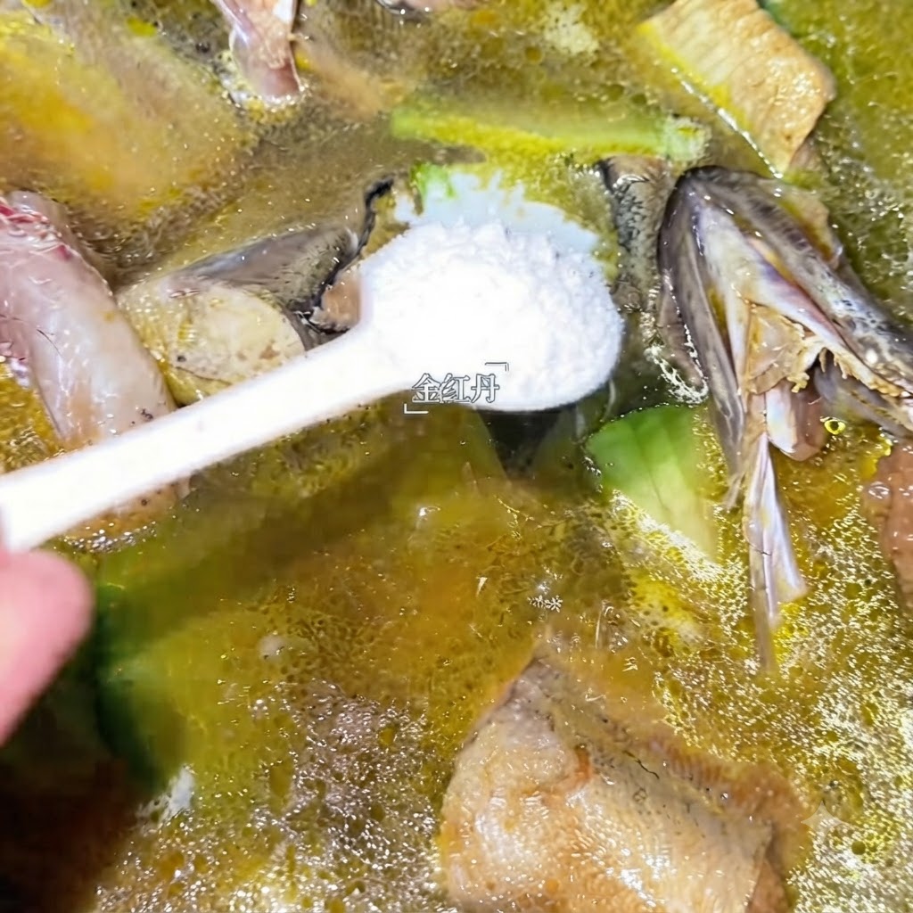 煮立っているタラスープの鍋に、スプーン一杯の白い調味料が加えられている状態。
