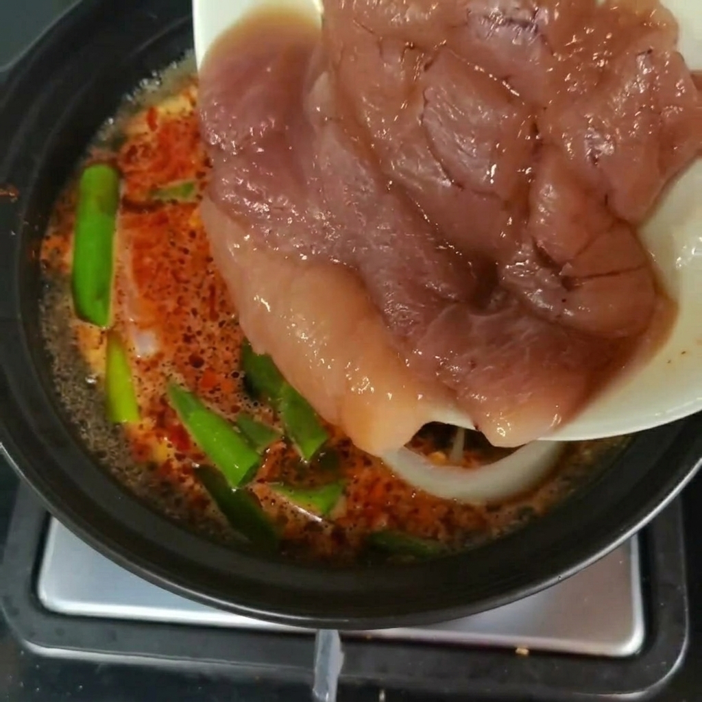 緑黄色野菜の入った煮込みスープの鍋に、皿から切り分けた新鮮な明太子を移し替えている様子。