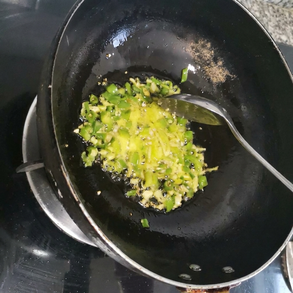 暗い色の中華鍋の中で、緑色の香味野菜と一緒に千切りにした赤唐辛子を炒め合わせている様子。