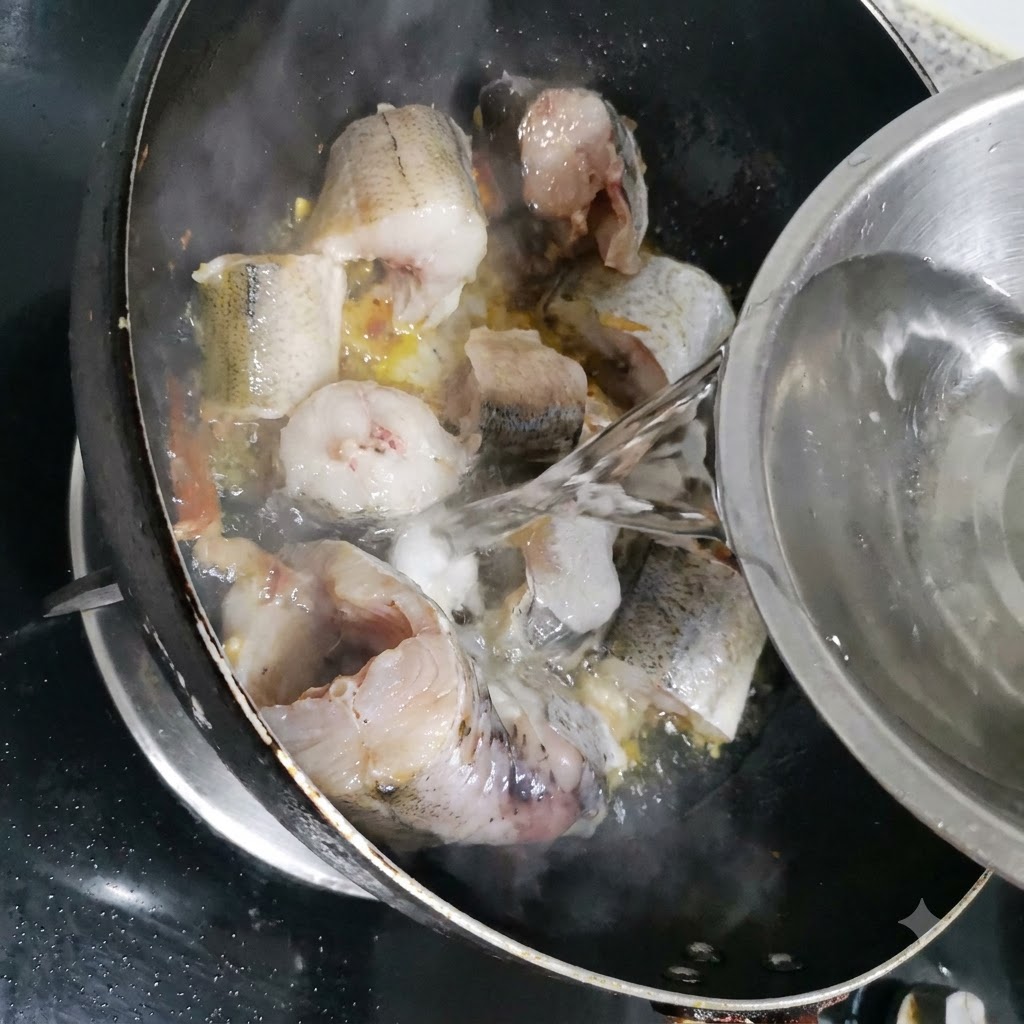 金属製のボウルから、スケソウダラの入ったフライパンへと水を注いでいる様子。