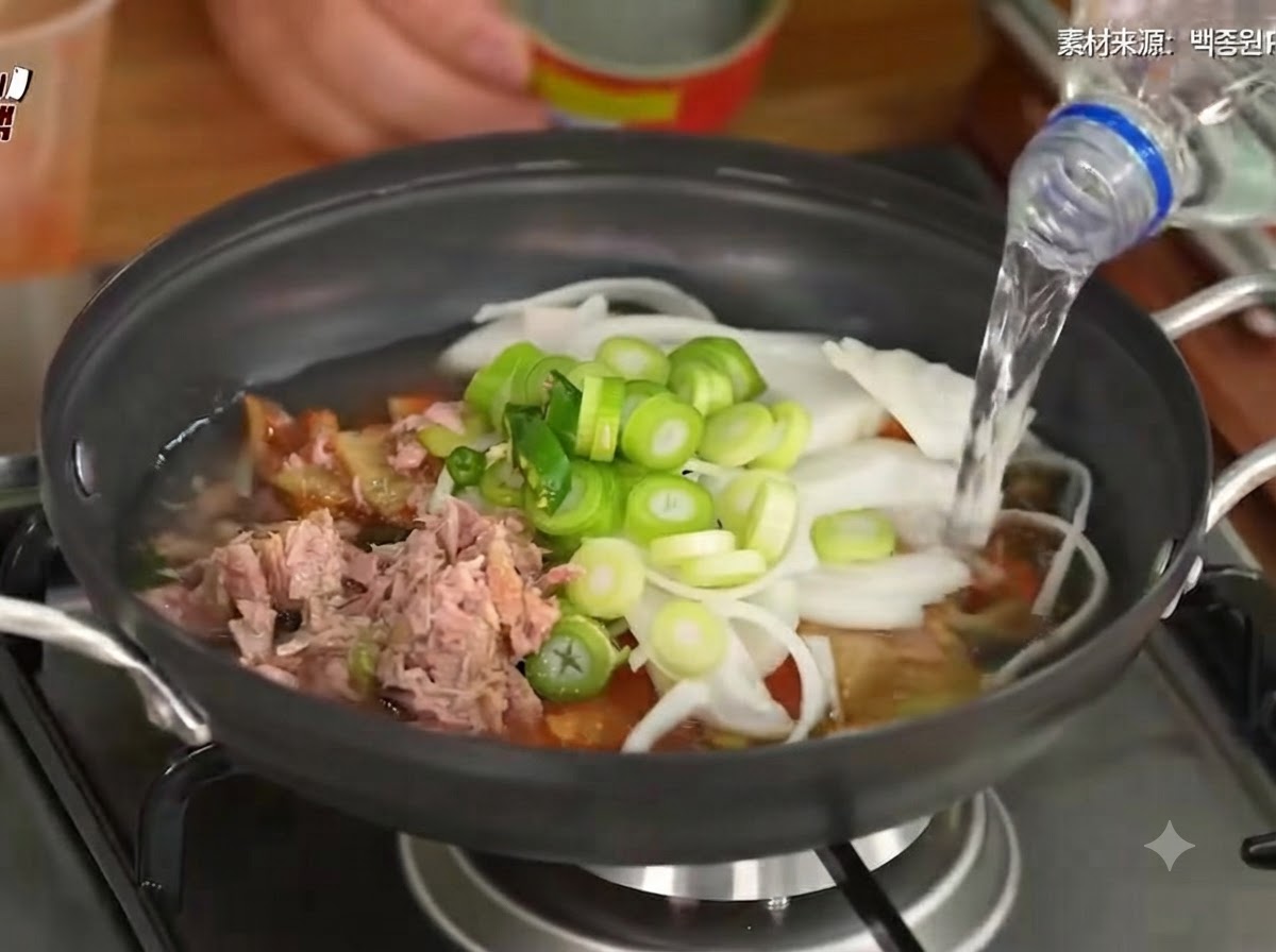 キムチ、野菜、ツナの入った鍋に水を注いでいる様子。