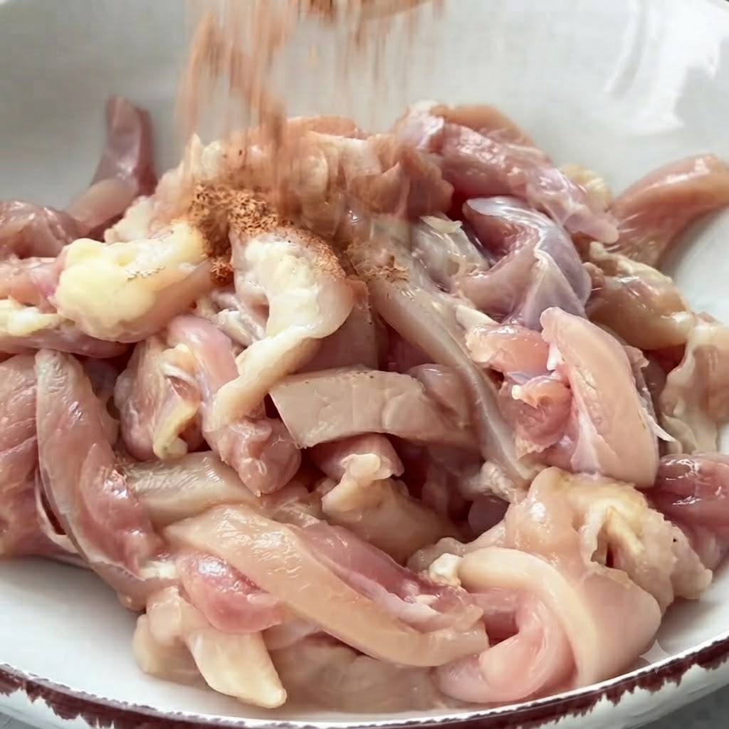 ボウルに入った生の鶏肉にスパイスを振りかけている様子。