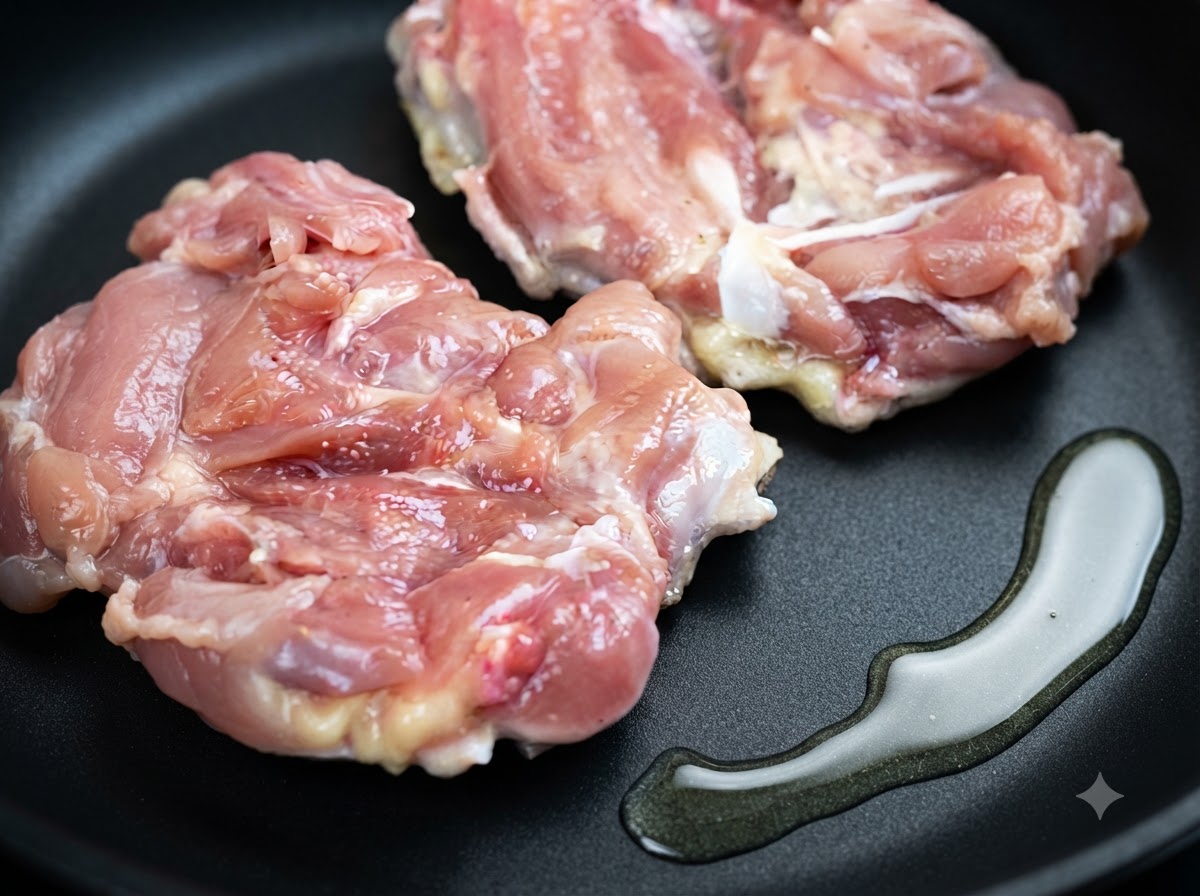 フライパンの中に、調理油のそばで置かれている2枚の生鶏もも肉の様子。