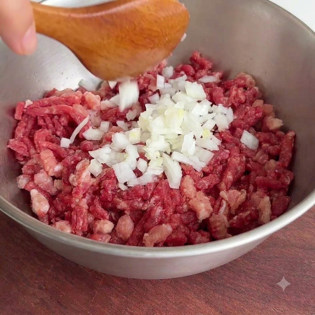 木製のスプーンを使って、新鮮な白い玉ねぎのみじん切りを生の牛ひき肉の入ったボウルに入れている様子