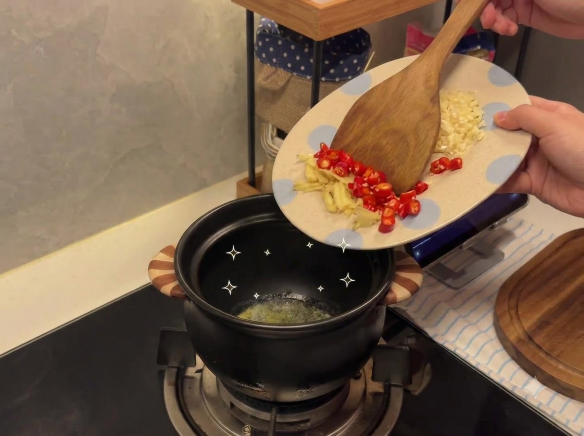 模様の入った皿から、溶けたバターの入った陶器の鍋へと、みじん切りのにんにくと唐辛子を移している様子。