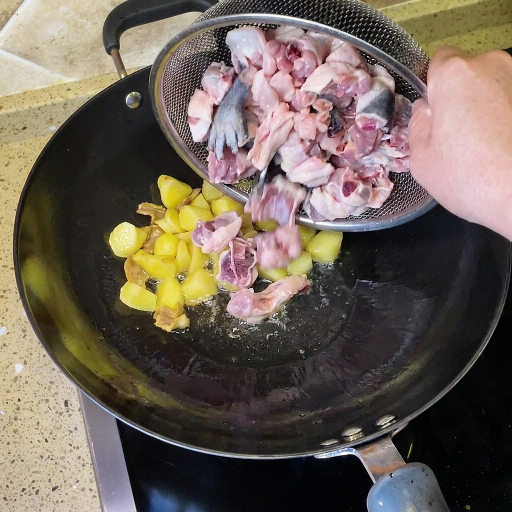 ざるに入った生の鶏肉を、生姜を炒めた中華鍋に加える様子