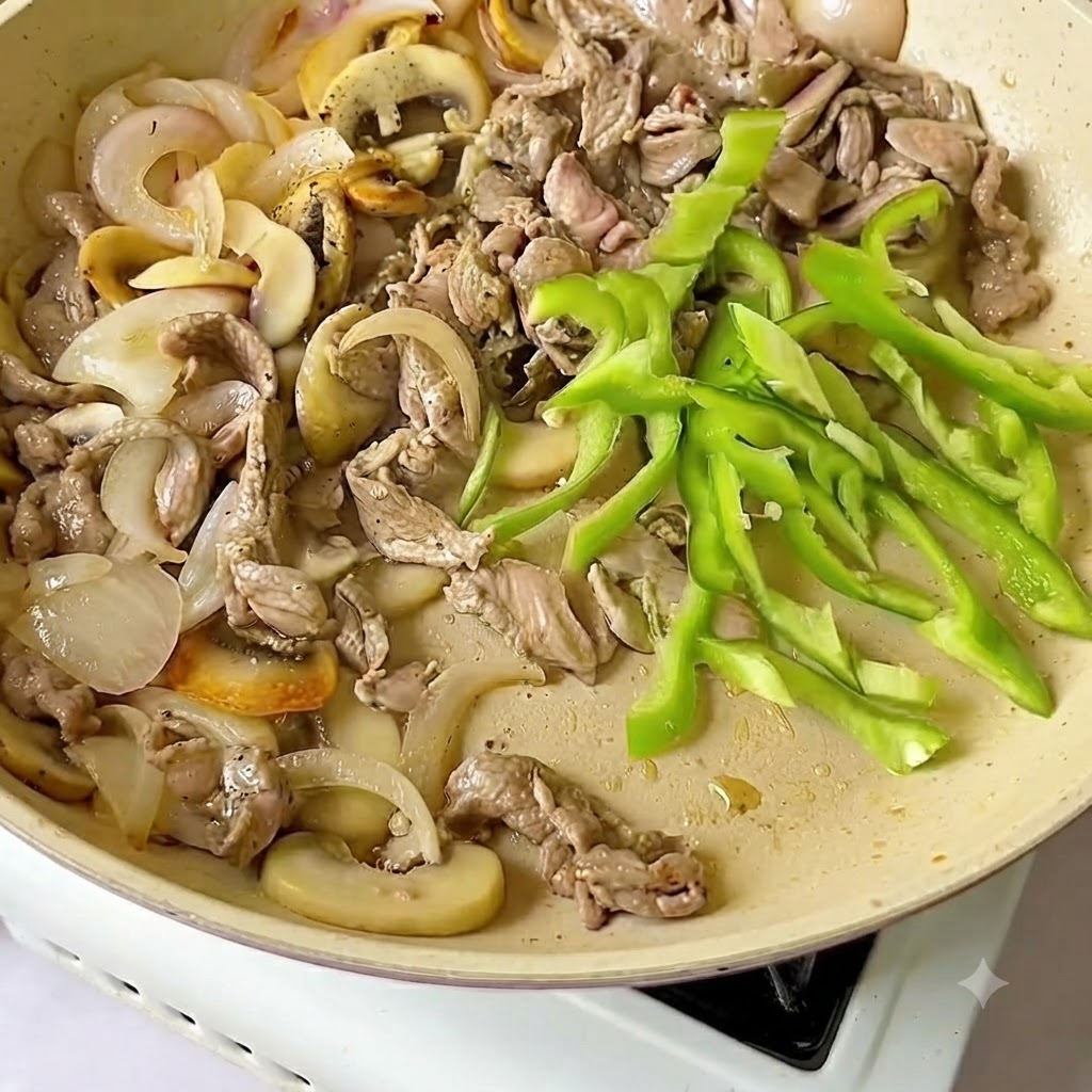 牛肉と玉ねぎが入ったフライパンに、新鮮な緑ピーマンのスライスが加えられている様子。