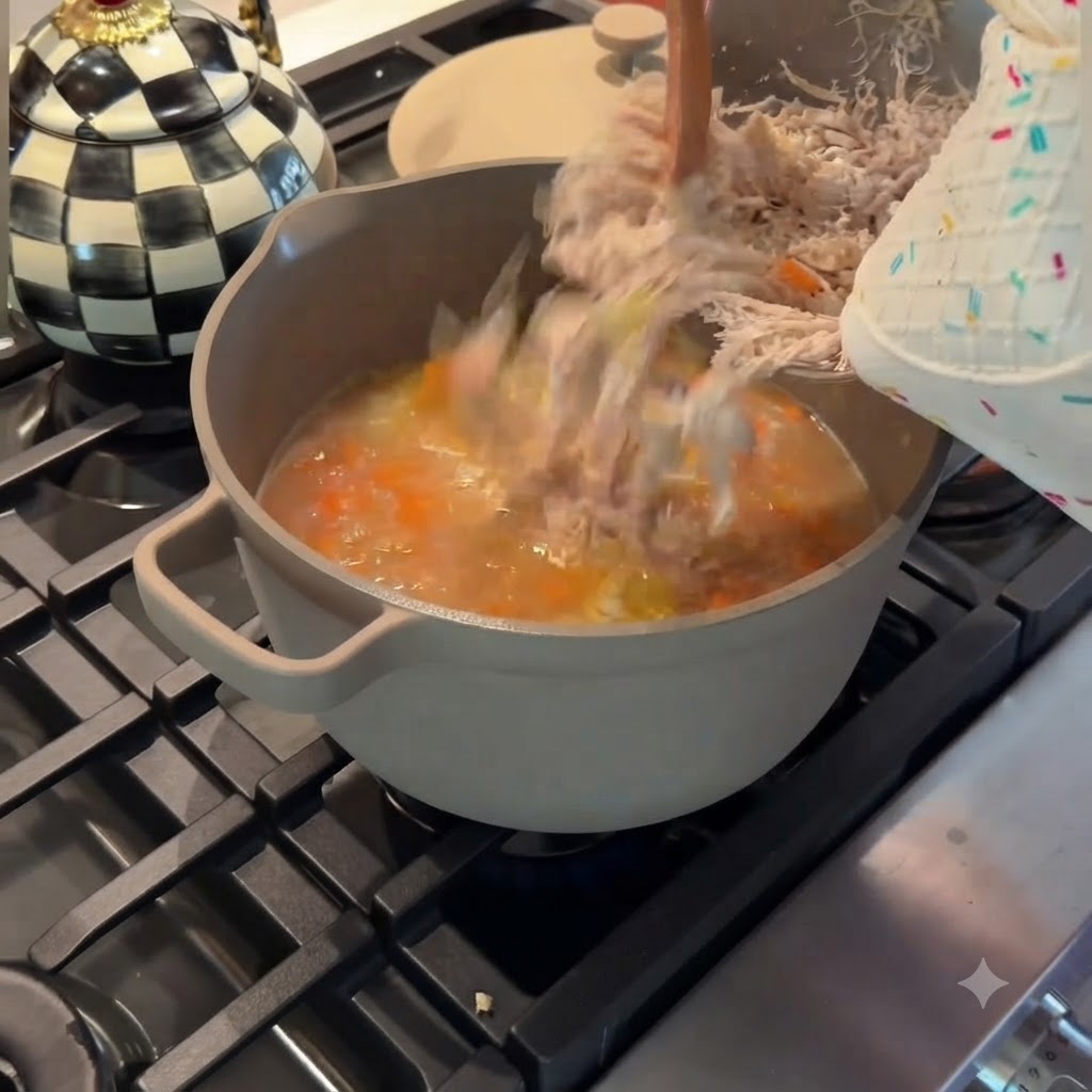 細かくほぐした鶏肉を、金属製のボウルから煮立っているスープの鍋に戻し入れている様子。