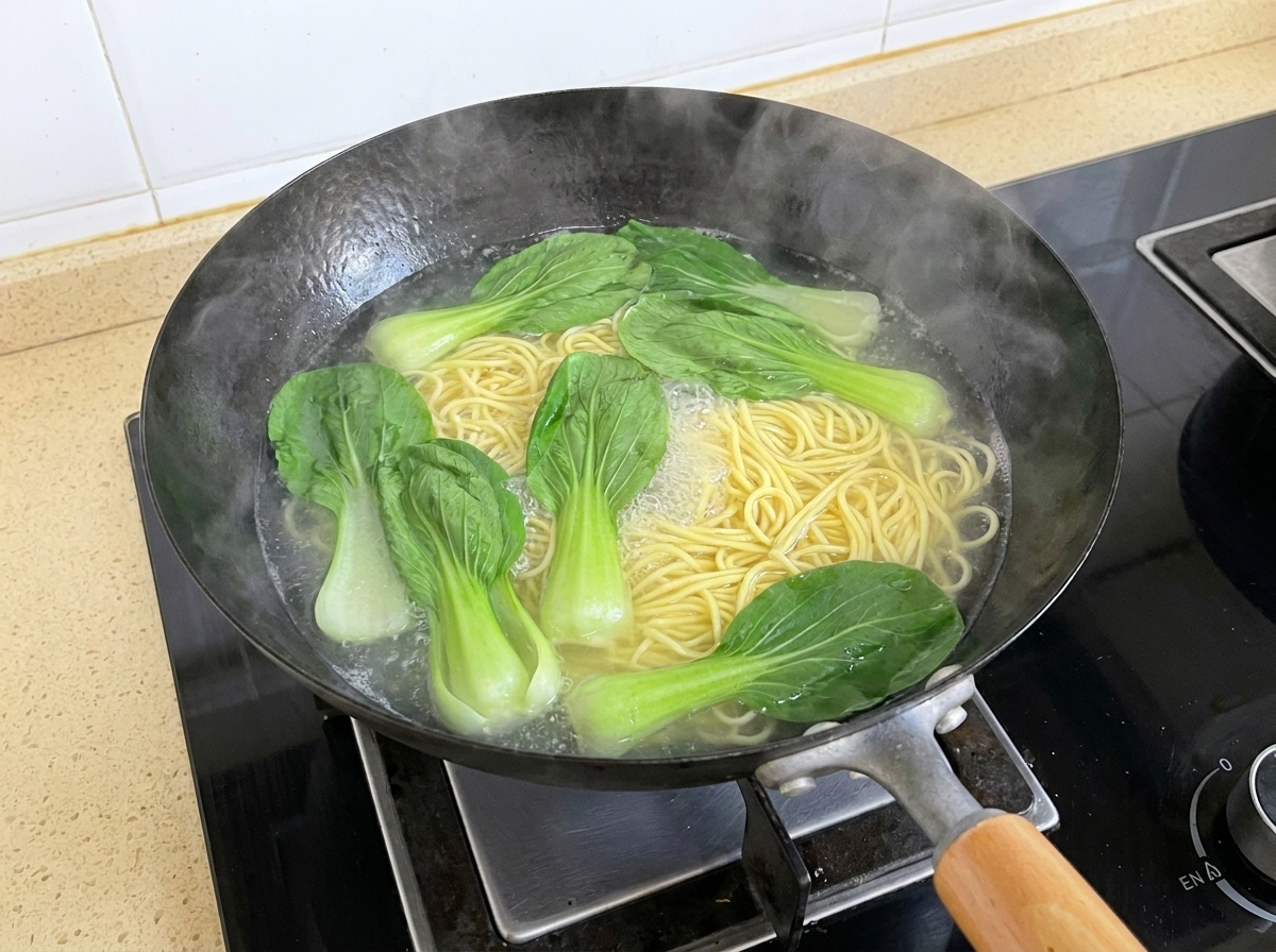 中華鍋で麺と一緒に沸騰したお湯の中で、緑色のチンゲン菜の葉が浮かんでいる様子。