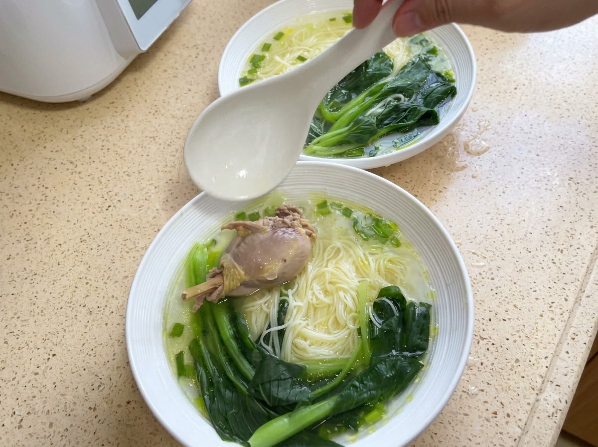 麺の上に鶏肉の塊と茹でたチンゲン菜がトッピングされているボウル。