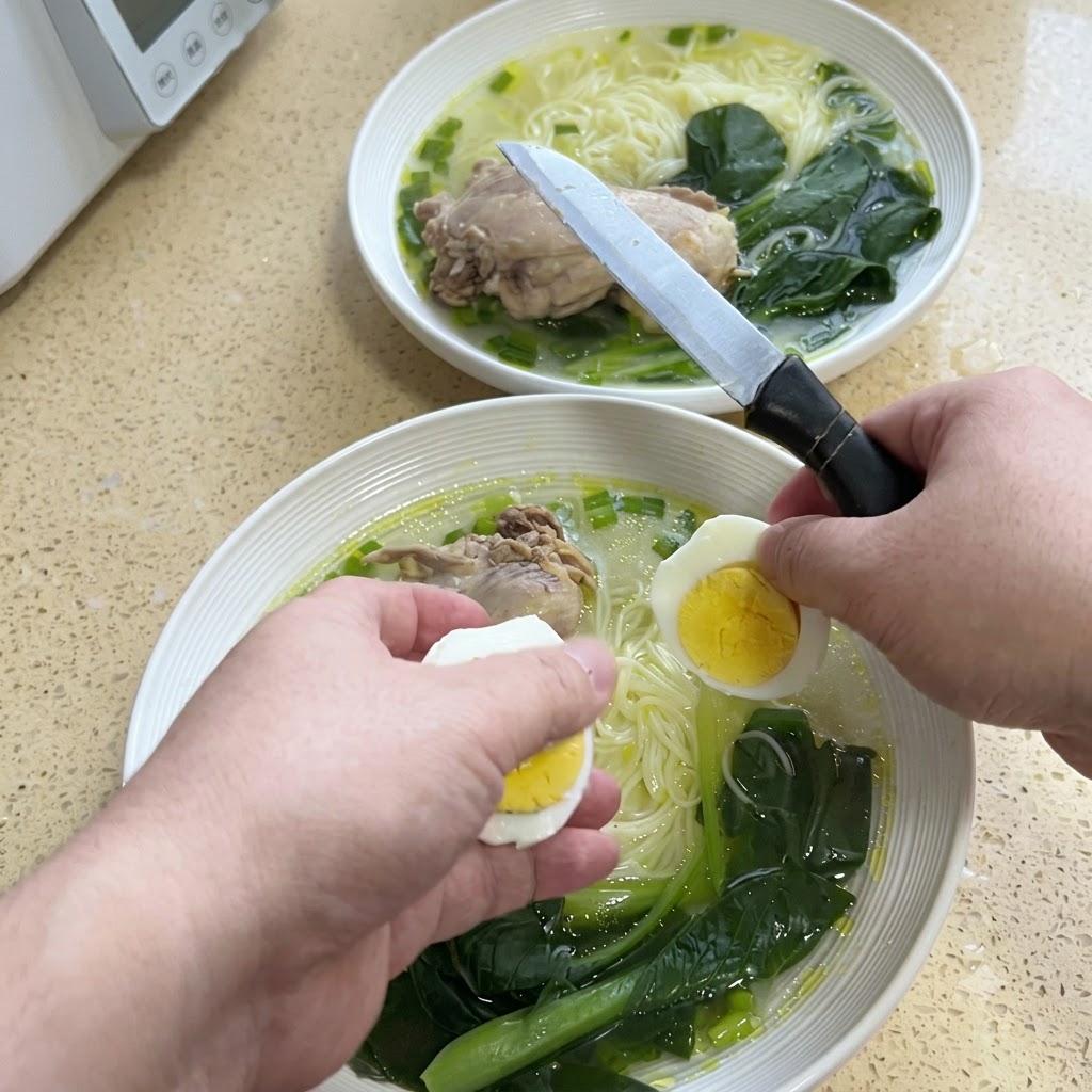 麺の入ったボウルの上で、手がナイフを使って固ゆで卵を半分にスライスしている様子。