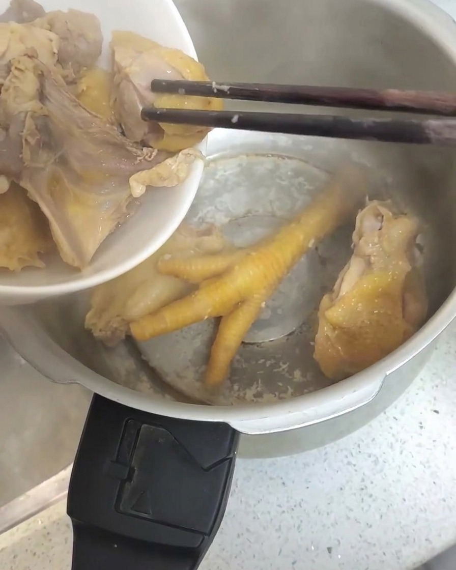 湯通しした鶏肉を、菜箸でステンレス製の圧力鍋に移している様子。