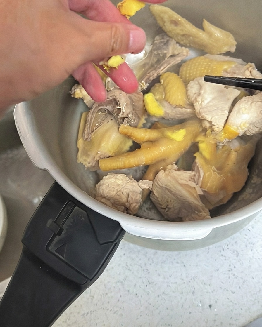 圧力鍋の中の鶏肉の上に、叩き潰した生姜を散らしている様子。