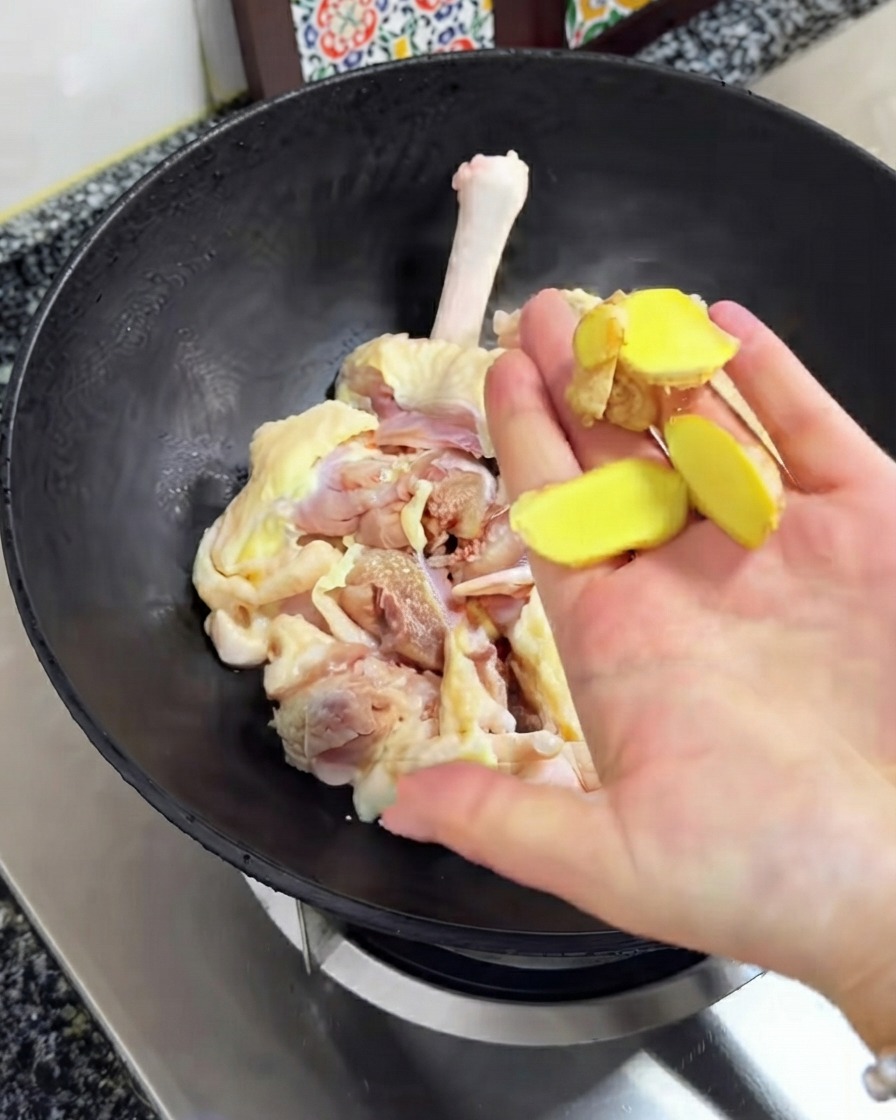 生姜のスライスが、黒い中華鍋の中にある生肉の上にかざされている様子。