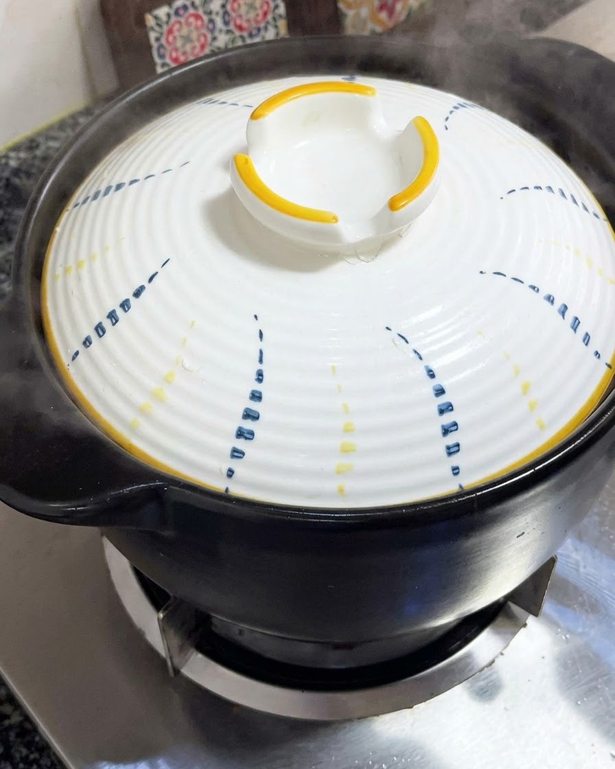 青と黄色の模様が入った白い蓋が、黒い土鍋の上にしっかりと置かれている様子。