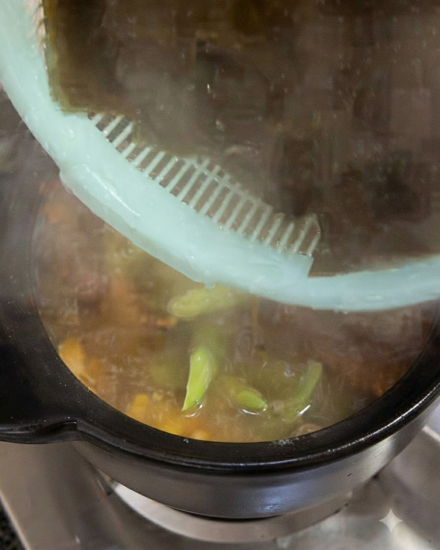 あらかじめ水で戻した濃い緑色の大きな昆布が、緑色のザルから調理鍋に入れられている様子。