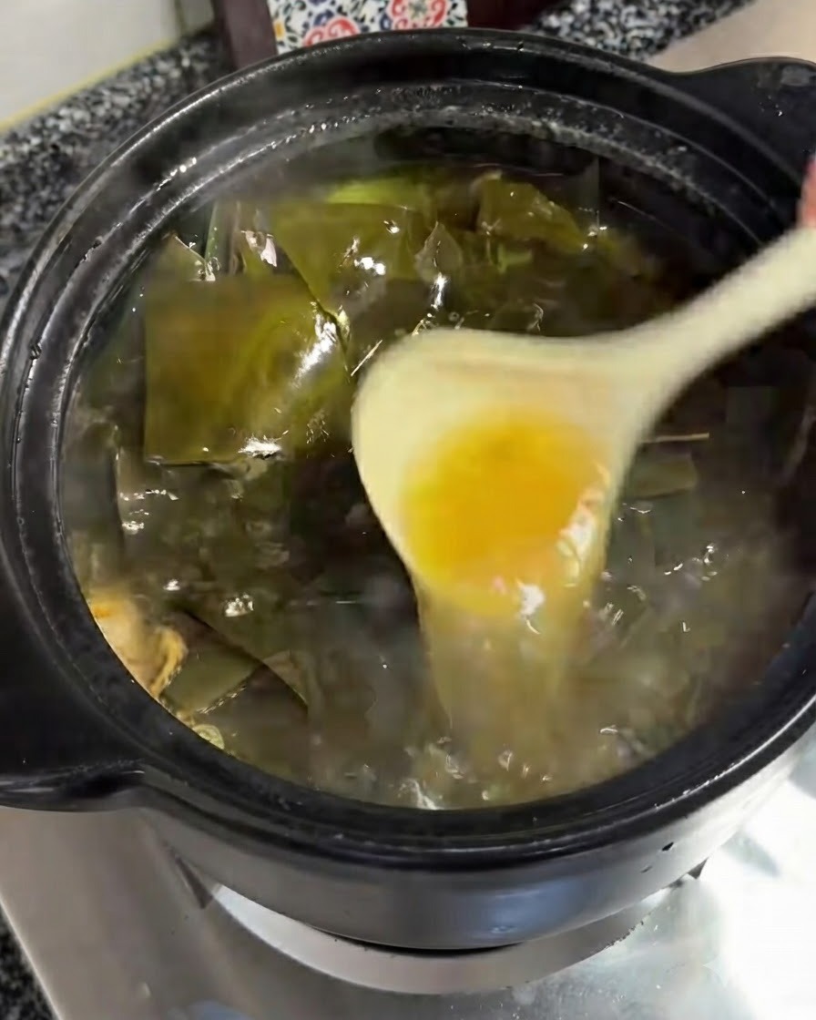 白いお玉を使って、スープの泡立つ表面から黄色っぽい油の層を取り除いている様子。