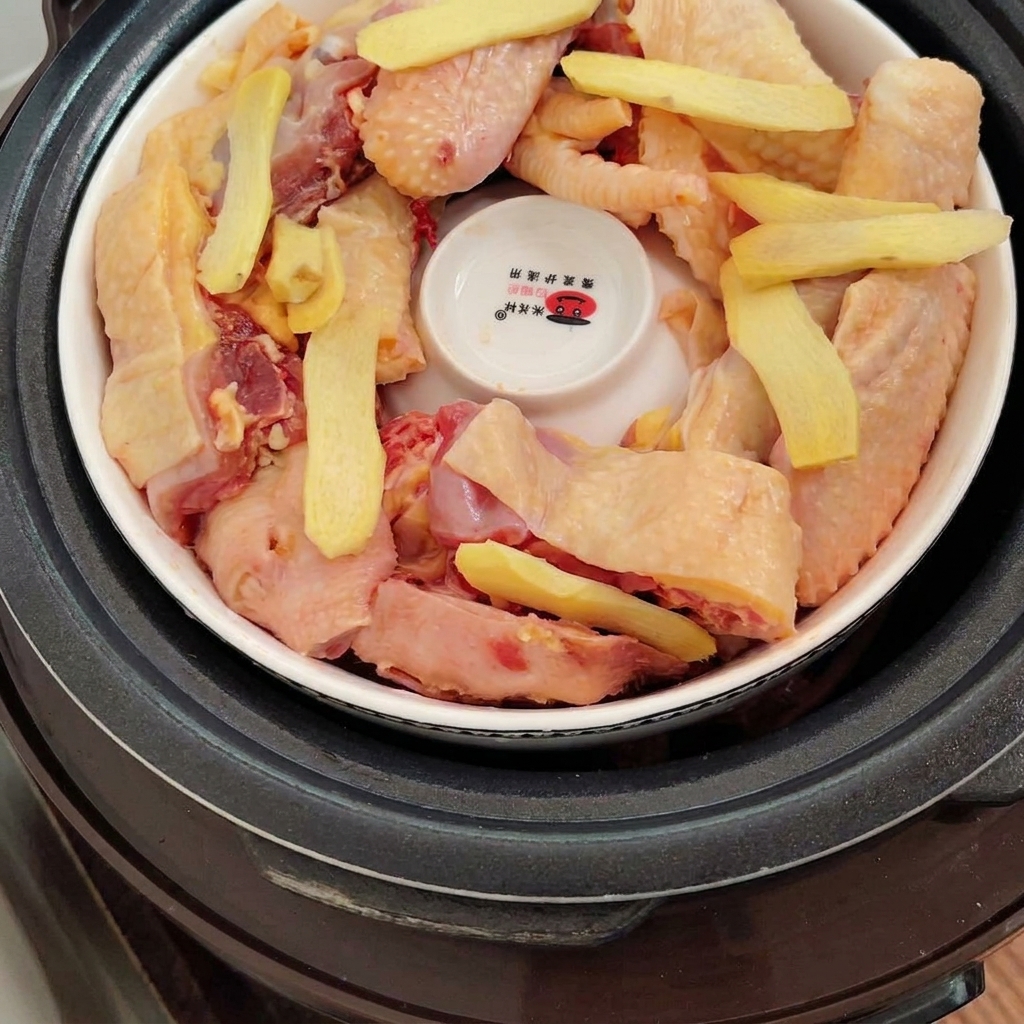 容器の中の鶏肉の上に、薄切りの新鮮な生姜が乗せられている様子。