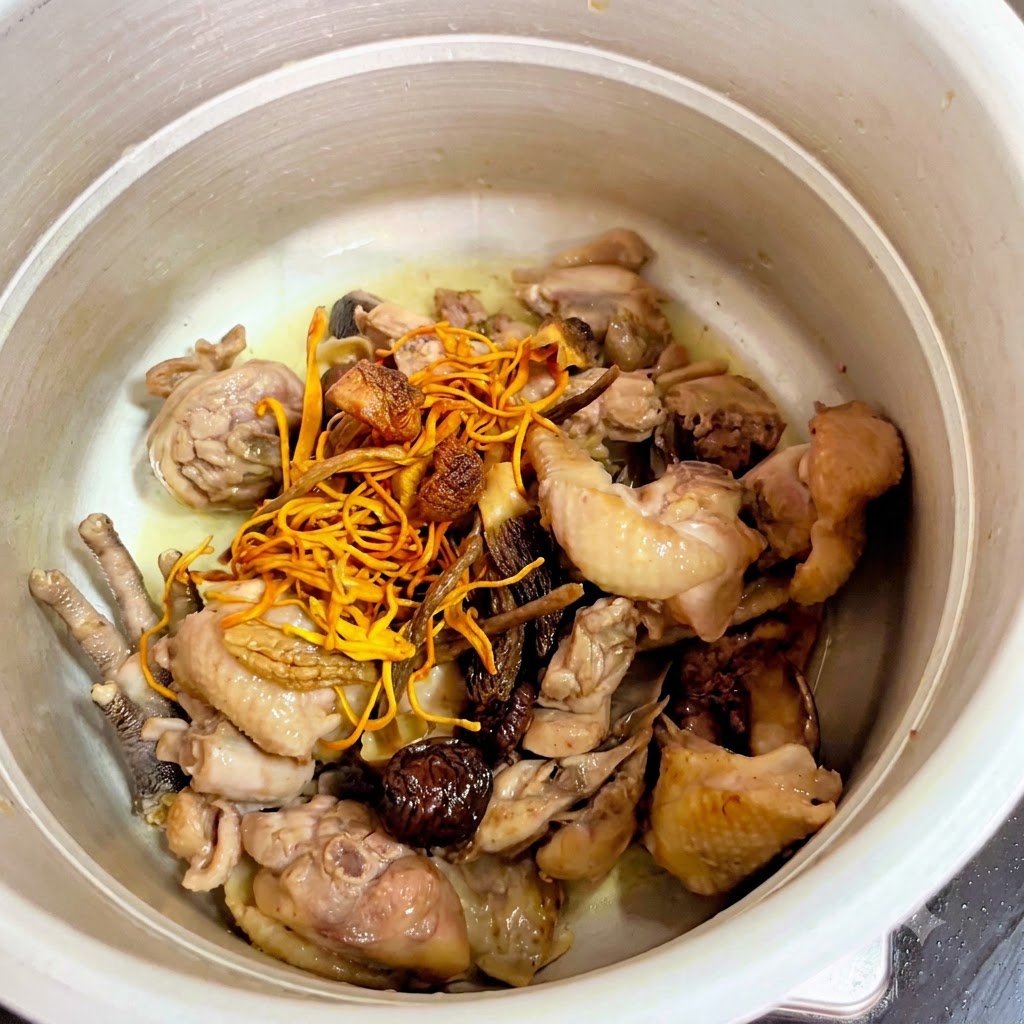 圧力鍋の中の鶏肉の上に乾燥キノコと黄色いサナギタケがのせられている様子