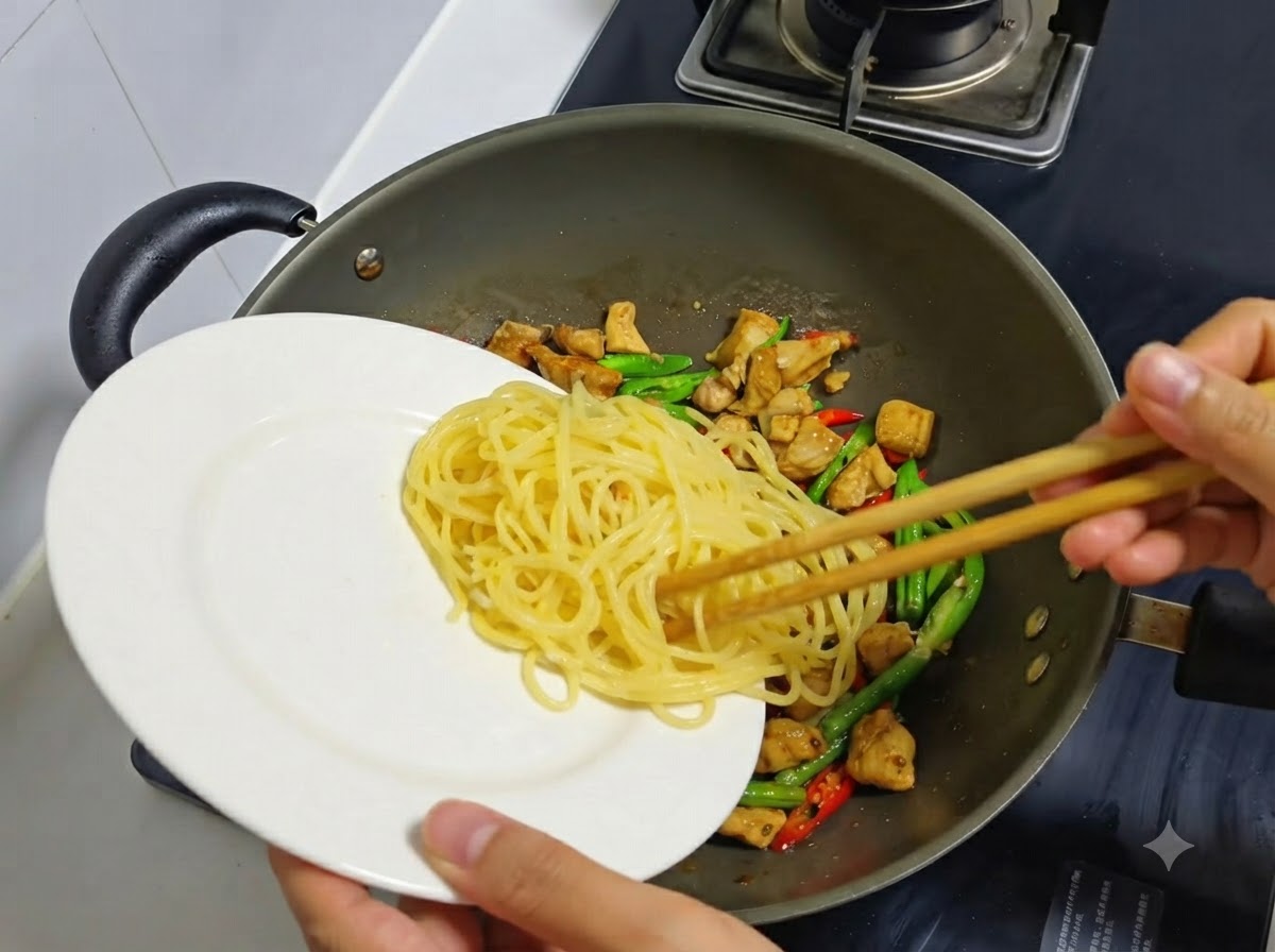 白いお皿に用意しておいた茹でたスパゲッティを、鶏肉と唐辛子が入った中華鍋に移し入れている様子。