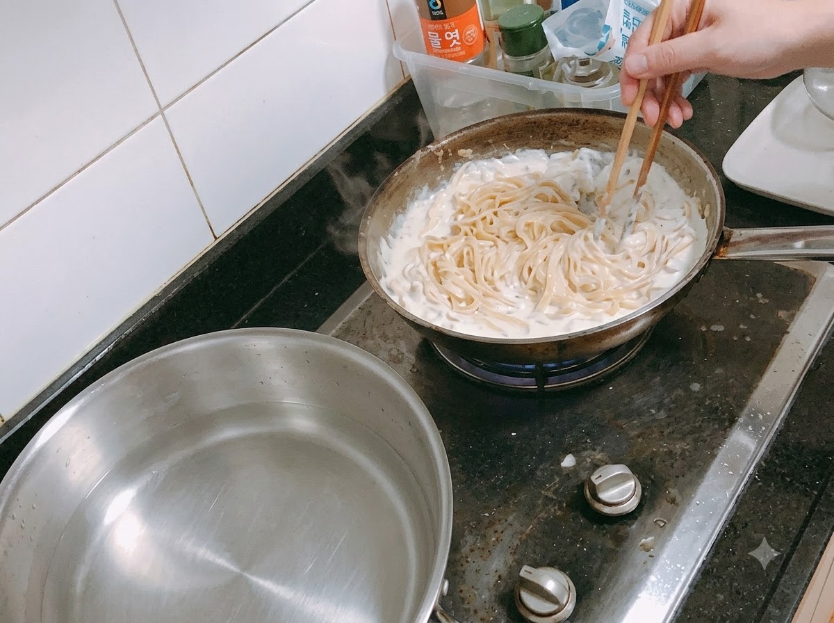箸を使って、とろみのあるクリームソースの中でパスタが和えられている様子。