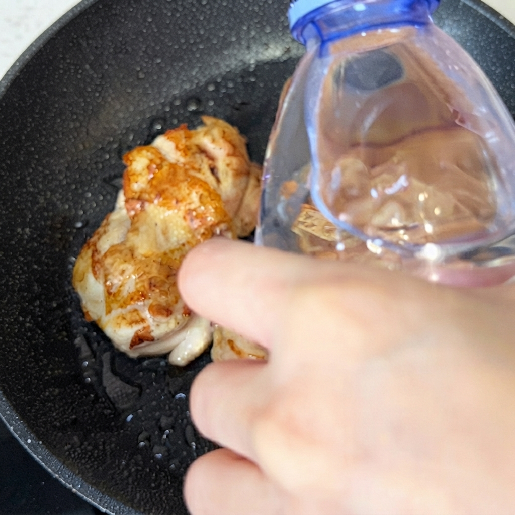 調理中の鶏肉が入ったフライパンに、ボトルから少量の水を注いでいる様子。