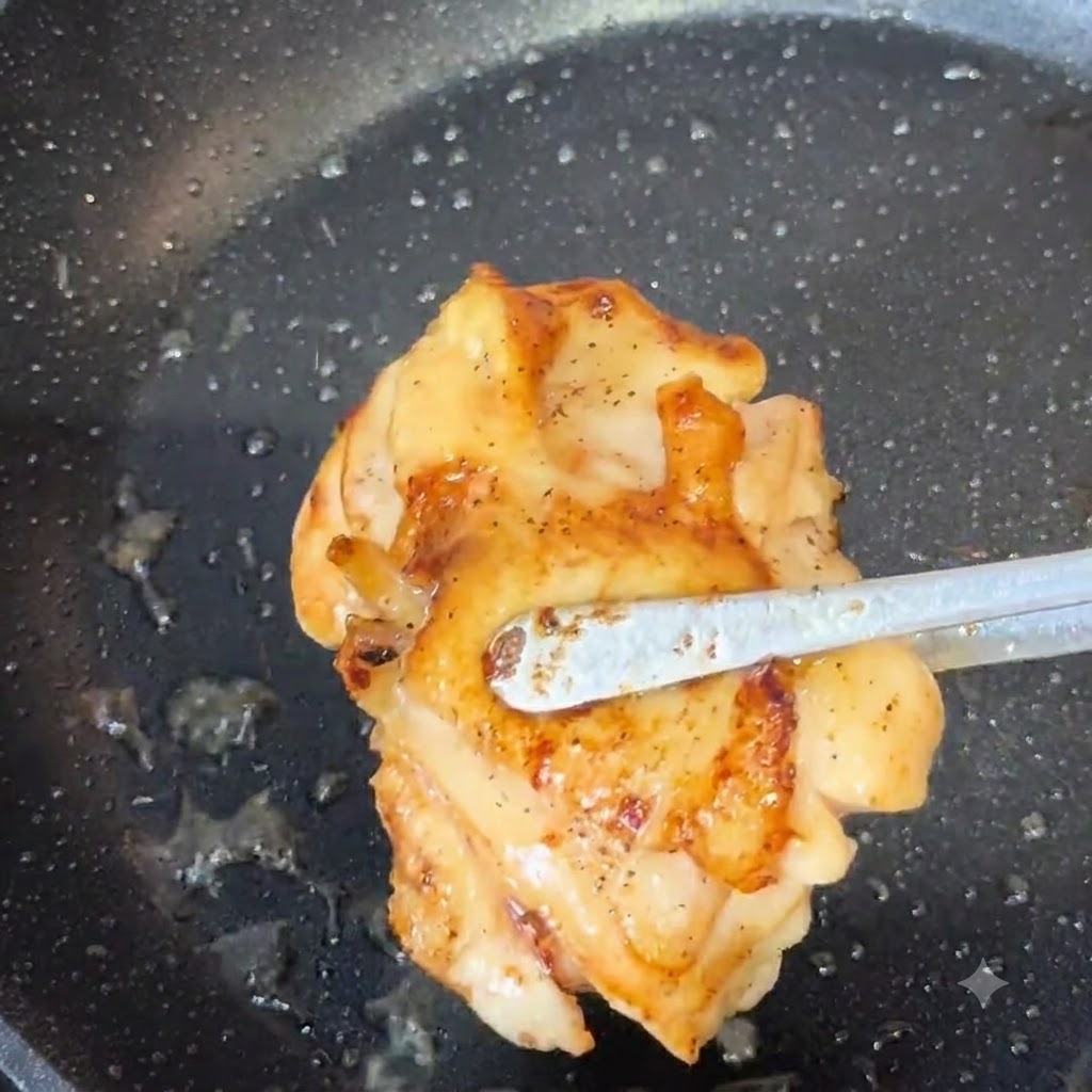トングを使って、きつね色に焼けた鶏もも肉をフライパンから持ち上げている様子。