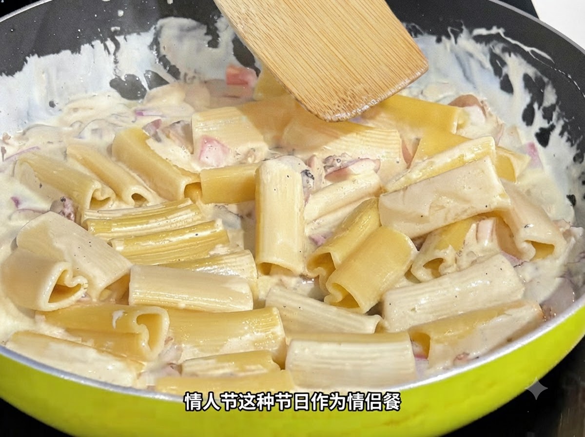 フライパンの中で、木製のスパチュラがハート型パスタをクリーミーなソースとともに混ぜ合わせている様子。
