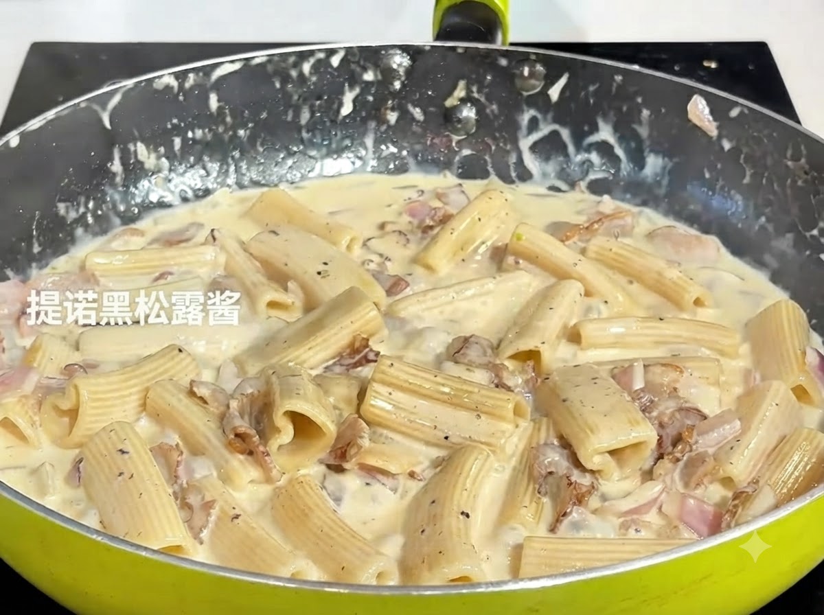 フライパンで煮込んでいるパスタの混合物に、スプーン一杯の濃い黒トリュフペーストを入れている様子。