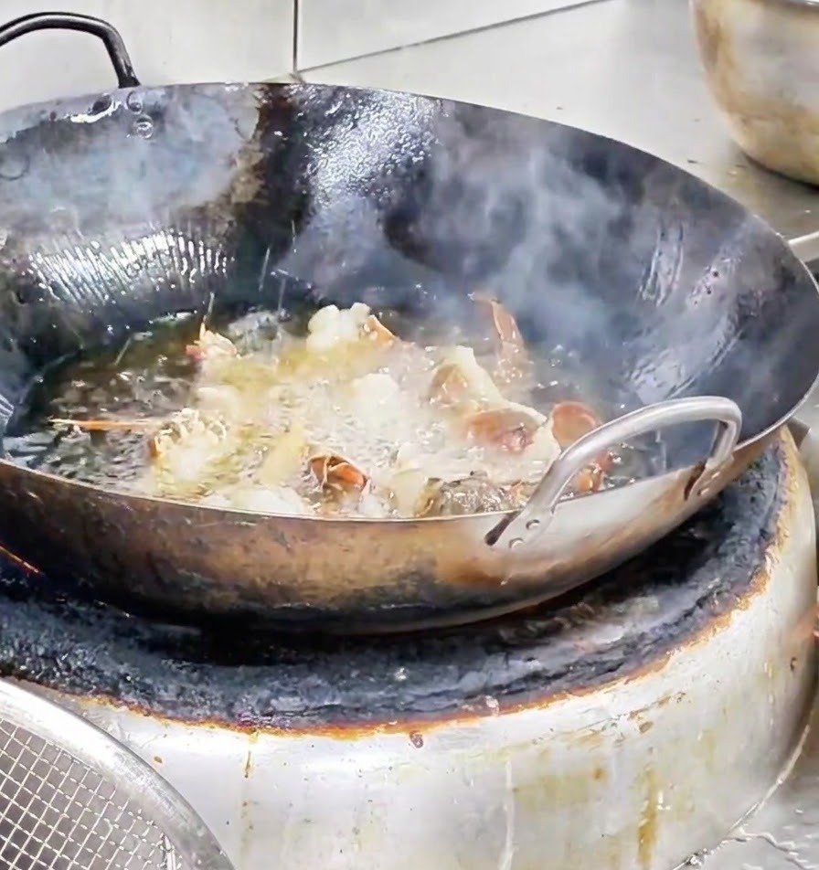 熱せられた油の入った中華鍋の中で、海老の切り身が激しく揚がっている様子。