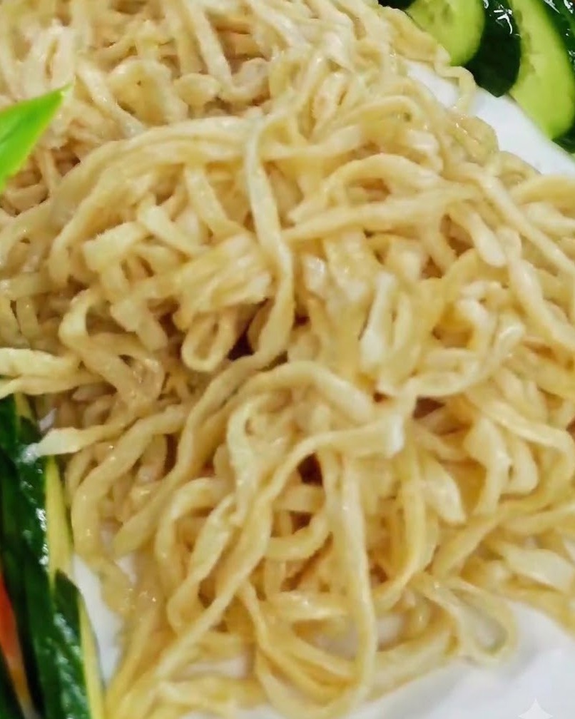 白いサービングプレートの麺の上に、調理した海老の切り身を丁寧に配置している様子。