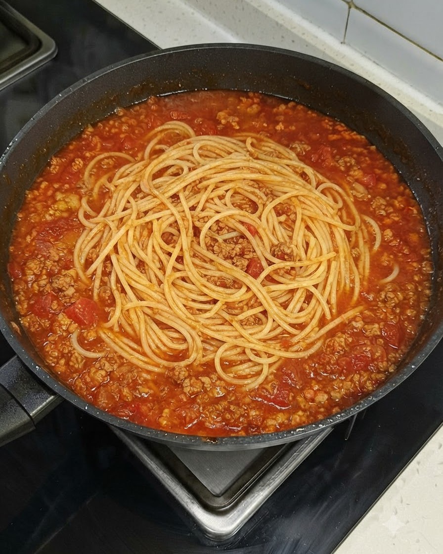 コンロの上の赤いミートソースで満たされた大きなスキレットの中央に、スパゲッティが綺麗に収まっているところ。