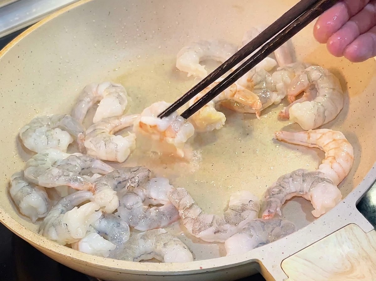 油を引いたフライパンで、ピンク色に火が通ったエビを菜箸で裏返している様子。