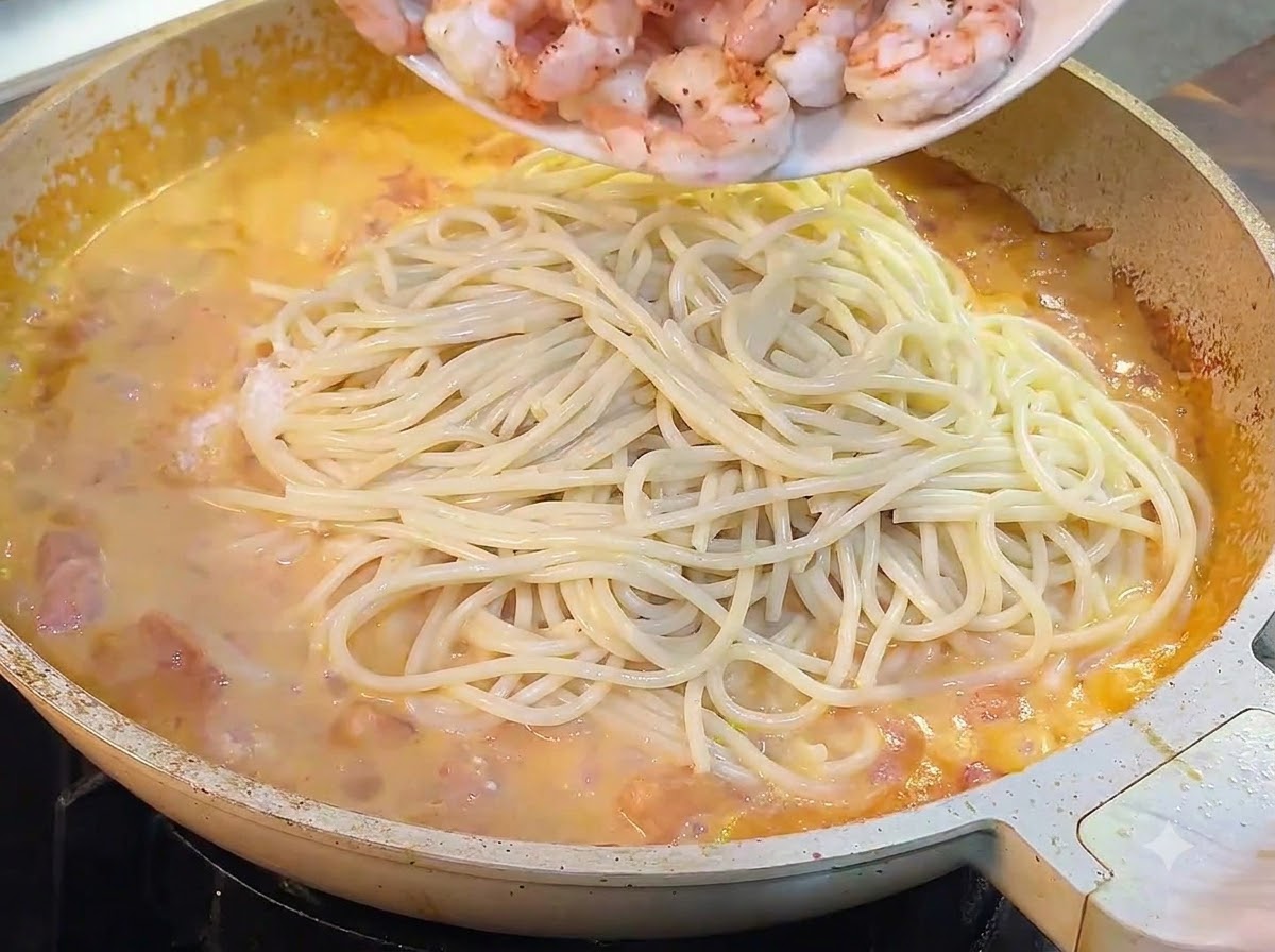 お皿に取り出しておいたエビを、スパゲッティとソースが入ったフライパンに戻し入れている様子。