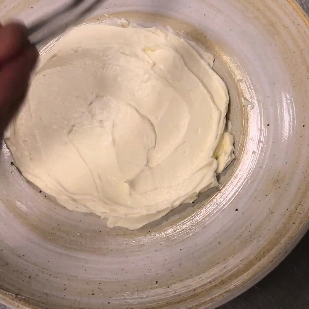 精密なキッチン用ピンセットを使い、広げたリコッタチーズの縁に沿ってミニトマトの半分を配置している様子。