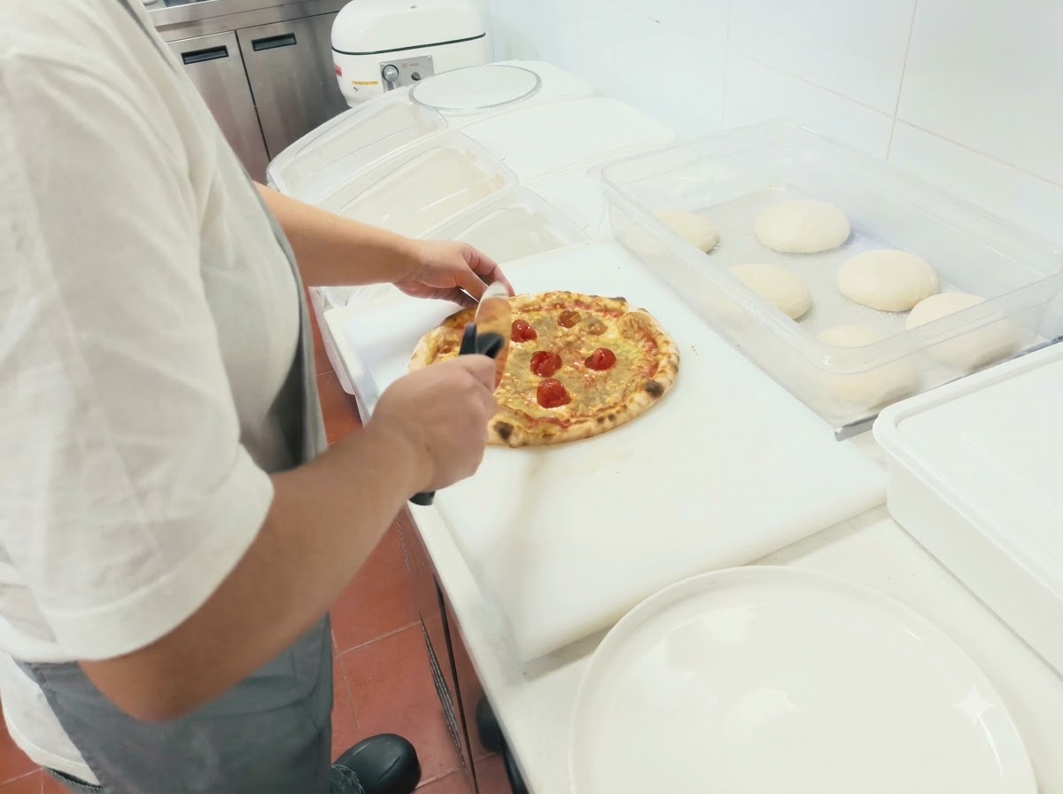 白いカッティングボードの上で、ピザカッターを使って焼き立てのピザを切っている様子。