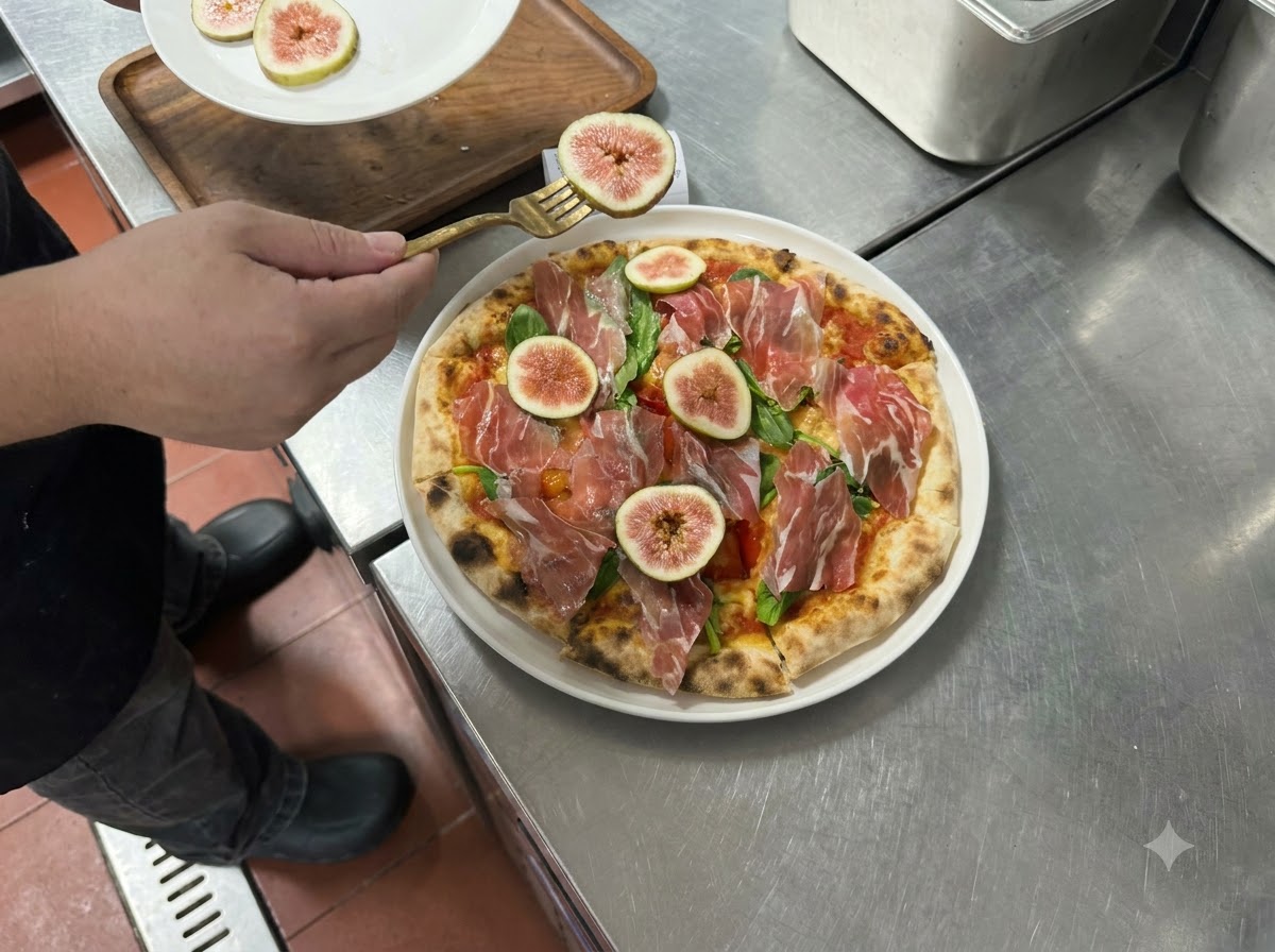 フォークを使って、焼き上がったピザの上に薄切りの生いちじくとプロシュートを並べている様子。