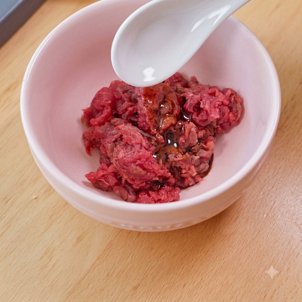 ピンクのボウルに入った角切り牛肉に白いスプーンで片栗粉を加えている様子。
