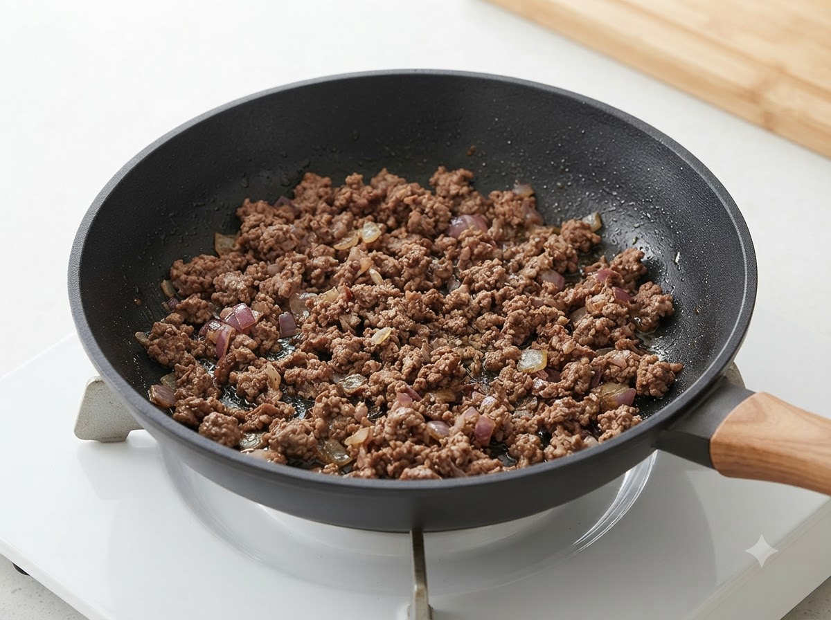 フライパンの中で炒めた玉ねぎと牛肉が混ざり合い火が通っている様子。