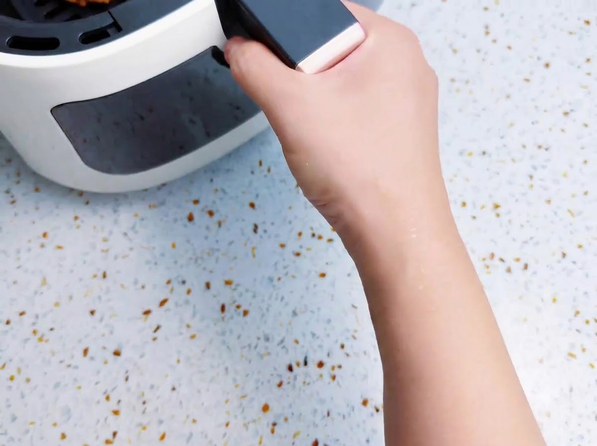 ベーコン巻きポテトスティックを入れたエアフライヤーのバスケットを本体に押し込んでいる様子。