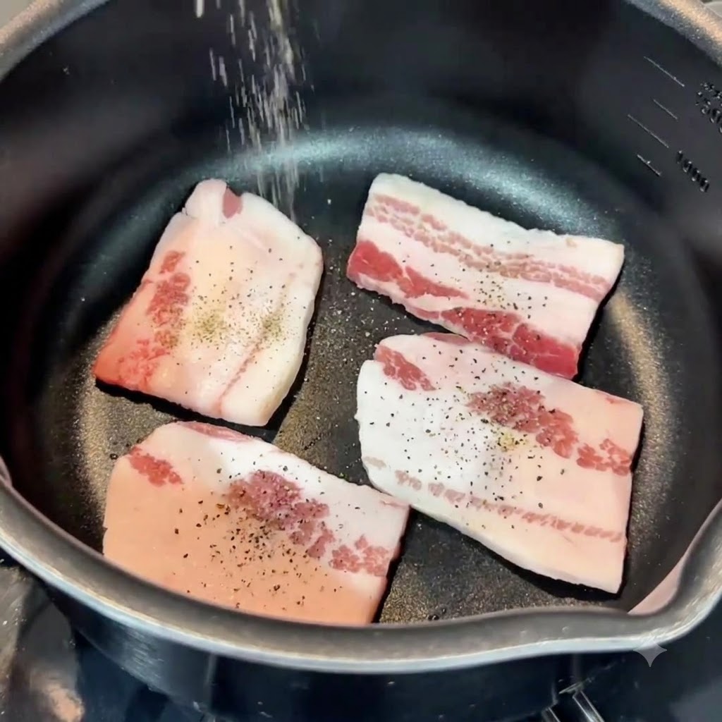 フライパンの中の豚バラ肉に、上から塩とこしょうが振りかけられている様子。