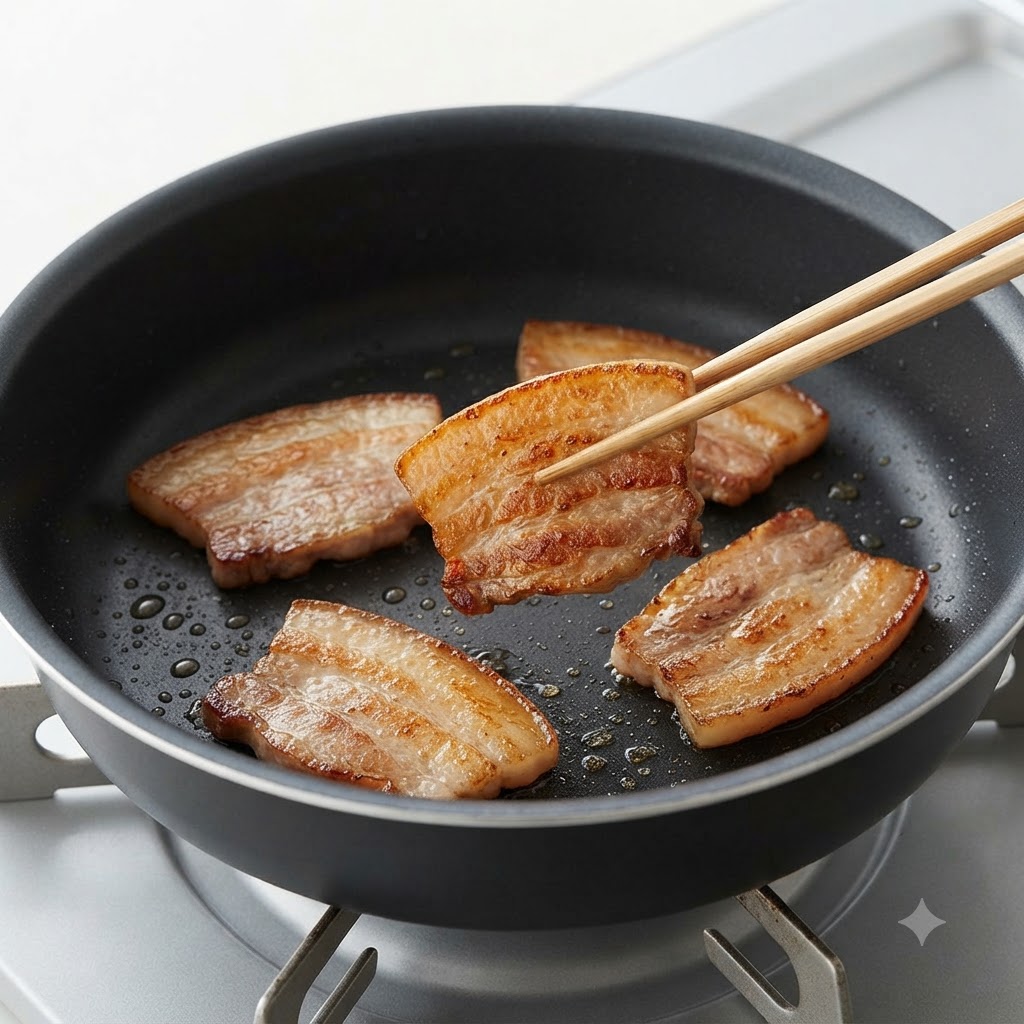 箸を使って、鍋の中で香ばしく焼き色がついた豚バラ肉を裏返しているところ。