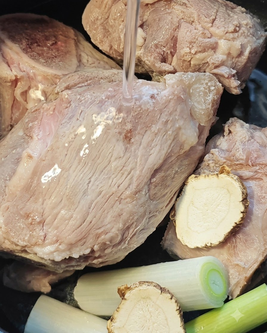 炊飯器の中で豚骨、トウキ、長ねぎの上から水が注がれる様子。