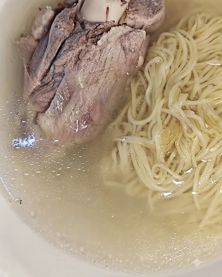 麺とスープの上に大きな豚骨がトッピングされた、完成したラーメン。