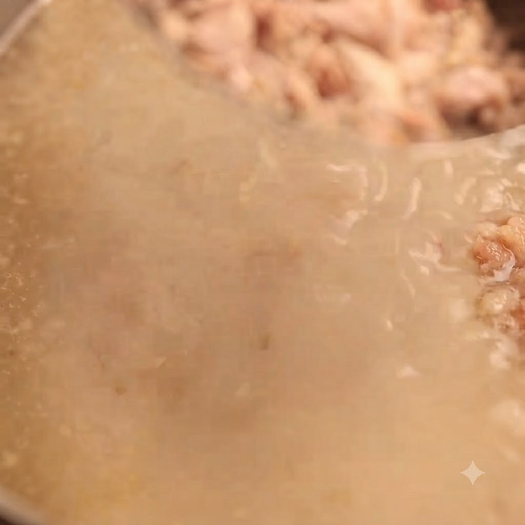 細かい肉片を濾すために、濃厚で乳白色の豚骨スープを目の細かいザルで漉している様子