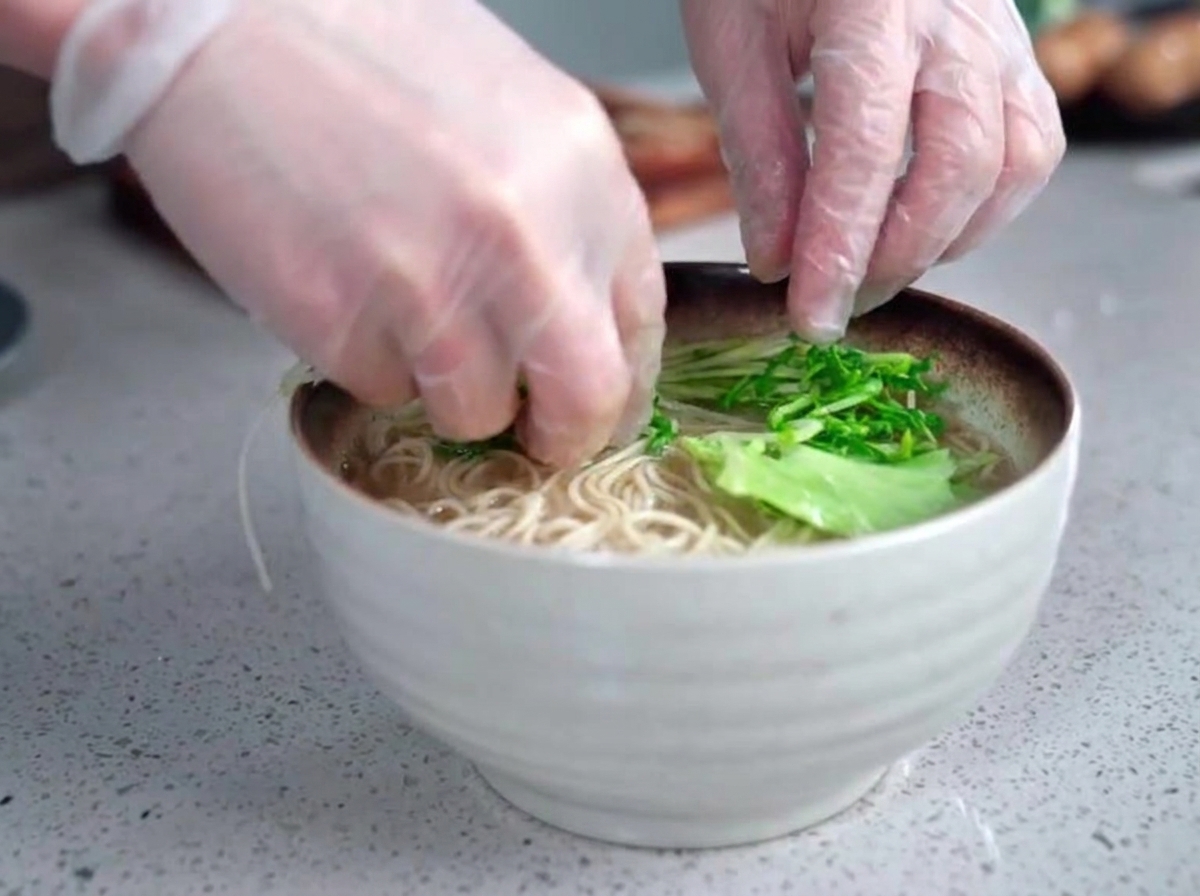 熱々のラーメン丼に茹でた青菜を丁寧に添えている手元