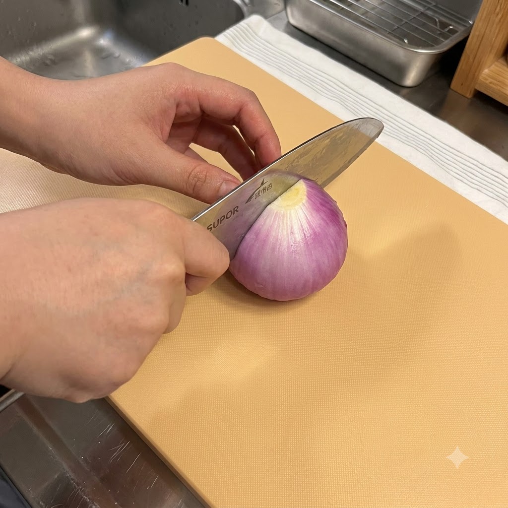 木製のまな板の上で、包丁を使って赤玉ねぎを切っている様子。
